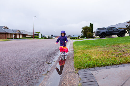 Happy child running and splashing through roadside gutter full of water on rainy autumn day