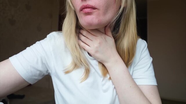 Blonde woman using throat spray to relieve pain. Close up of female treating sore throat or seasonal illness with medication at home.