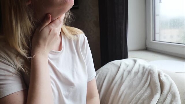 Blonde woman using throat spray to relieve pain. Close up of female treating sore throat or seasonal illness with medication at home.