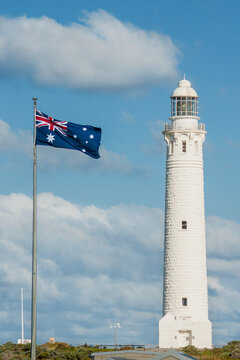 The historic Cape Leeuwin Lighthouse standing next to an Australian flag flying on a flagpole