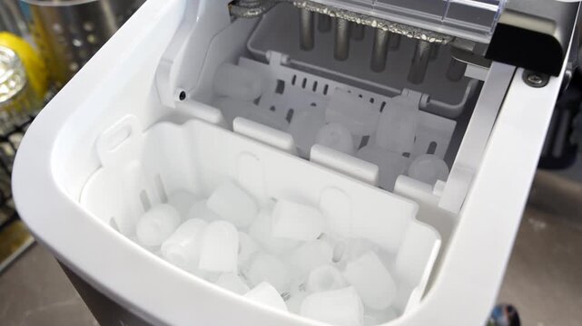 Close-up of portable countertop ice maker producing fresh ice cubes, summer drinks and home kitchen.