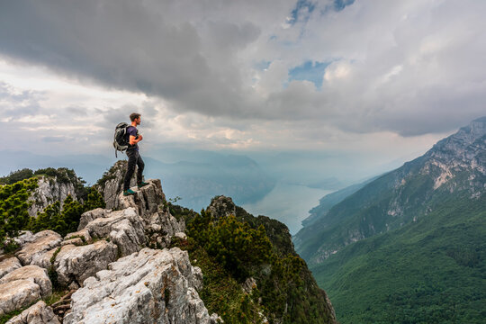 Hiker standing on a mountain cliff, embracing outdoor adventure and travel freedom with panoramic views over Lake Garda, Ventrar trail, Monte Baldo Natural Park, IBrentonico,Trentino,Veneto Italy.