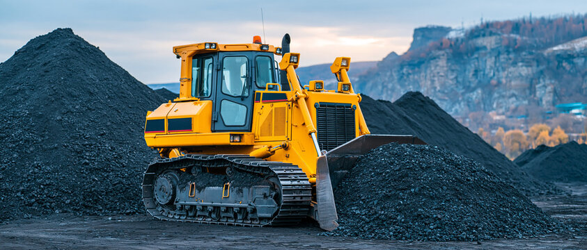 Heavy yellow bulldozer moving piles of black coal against a rugged mountain backdrop.