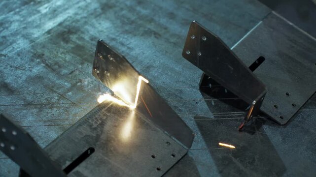 Laser cutting metal brackets with molten seam, sparks, and smoke in workshop showing precise industrial fabrication on worn steel surface under focused light, with laser, cutting, metal, bracket