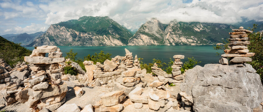 Stone cairns placed on a mountain ridge overlook Lake Garda, highlighting an outdoor tourism destination and nature adventure, Arco, Trentino, Veneto, Italy.