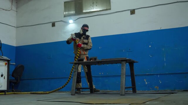 Protective technician repositions corrugated hose beside clamped steel pieces on metal workbench inside industrial workshop with cool overhead light and worn surfaces