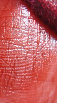 Detailed macro view of a woman applying glossy red lipstick, focusing on the vivid pigment and flawless skin texture for a beauty concept.