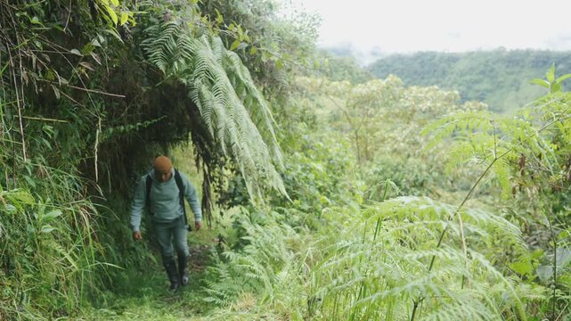 Latino man walking in the mountains, trek wearing rubber boots and a cold-weather beanie hat in tropical landscape 
