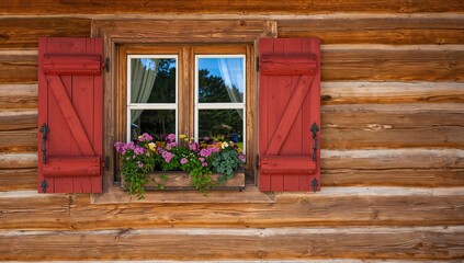 Obraz premium Wooden Cabin Window with Red Shutters and Flower Box in Daylight