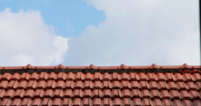 Terracotta Roof Tiles Under a Cloudy Sky: A close-up view of traditional terracotta roof tiles under a bright blue sky filled with fluffy white clouds, offering a sense of home and shelter.