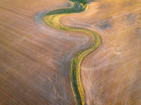 Aerial view of a green fertile gully snaking through a dry ploughed paddock