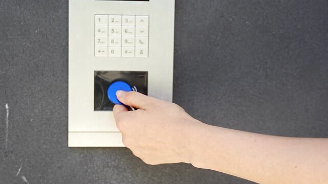 Person using contactless key fob on residential building access control system. Secure entry technology supports convenient and controlled property access