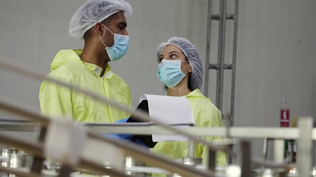 Supervisory team wearing PPE meticulously inspects the mackerel or sardine production line from canning to tomato sauce filling on conveyor belts in industrial seafood processing plants.