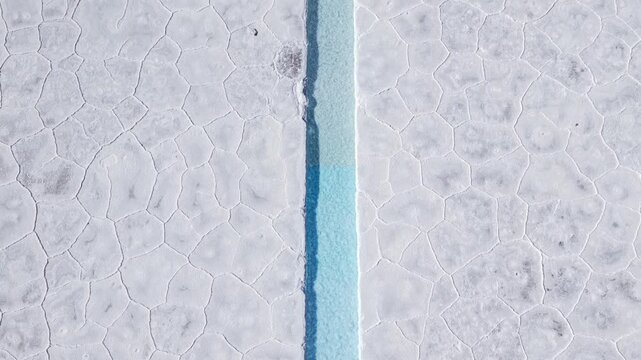 Drone aerial video of turquoise salt channels and white salt flat rows in Salinas Grandes, Argentina.