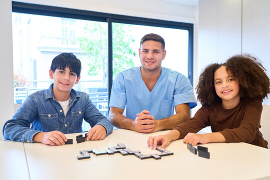 Pediatric Physiotherapy Session with Therapist and Children Playing Dominoes, Rehabilitation Exercises for Motor Skills Training, Pediatric Rehab Center, Smiling and Engaged
