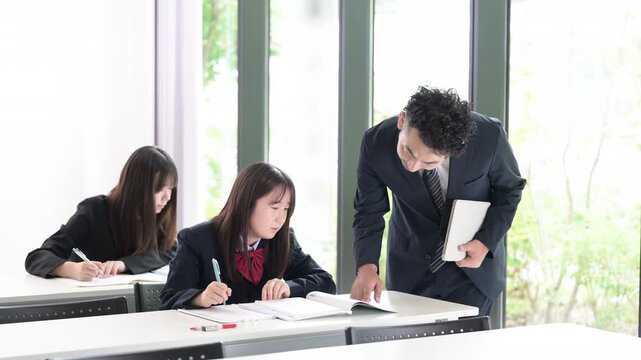 塾や学校の教室で個別指導を行う教師と勉強に取り組む日本人女子中学生や女子高校生　予備校や高校の授業風景　集団や個別塾などのイメージの動画