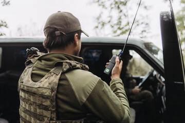 Fototapeta premium Ukrainian soldier communicating by radio near military vehicle