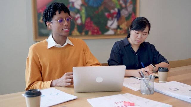 Diverse young colleagues working together on laptop computer in modern office, business collaboration concept