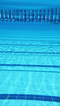 Empty indoor swimming pool lane underwater view with blue reflections.