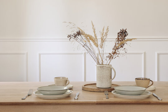 Minimalist Elegant Dining Table Setting with Ceramic Tableware, Coffee Tea Cup, Cutlery. Dried Grass in Vase Arrangement. Neutral Scandinavian Home Interior Decor. Living Room, Beige Wall background.