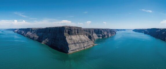 Fototapeta premium Panoramic View of Steep Rocky Cliffs Overlooking Turquoise Water Under Clear Blue Sky
