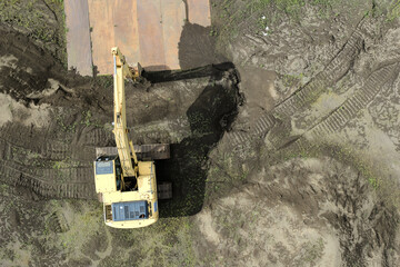 Top-down drone view of a hydraulic excavator performing earthworks at a construction site © sorao yamao