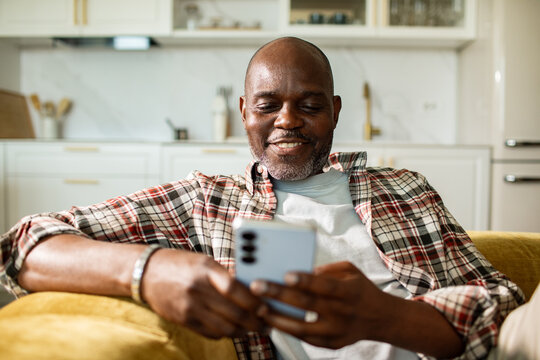 Smiling man using smartphone on sofa at home