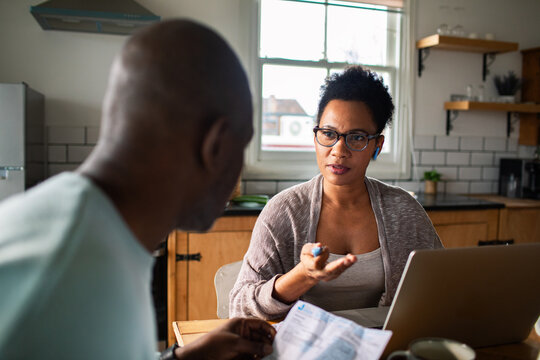 Mature couple discussing household finances with laptop at kitchen table
