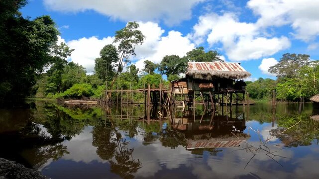 Wooden stilt house reflecting on calm amazon river water surface