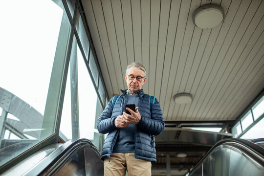 Senior man using smartphone on escalator at train station