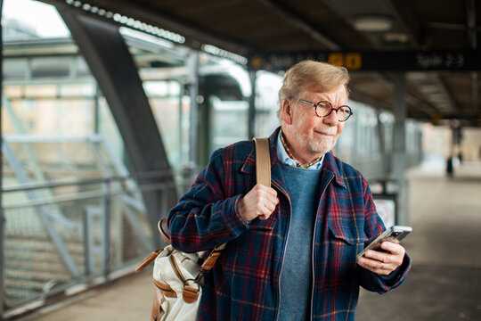 Senior traveler checking smartphone at train station