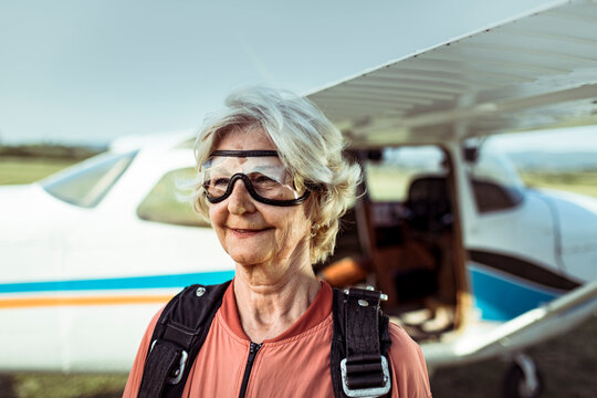 Senior woman skydiver smiling by small airplane at airfield