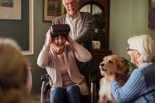 Senior friends laugh as woman in wheelchair tries vr headset at home