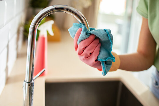 Person cleaning kitchen faucet with microfiber cloth at home