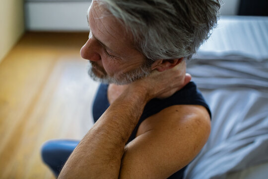 Middle-aged man rubbing sore neck in bedroom