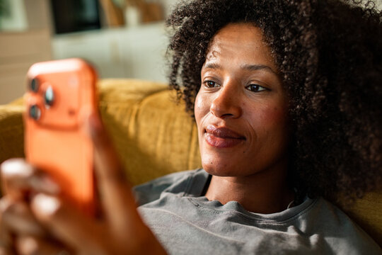 Woman relaxing on sofa using smartphone at home