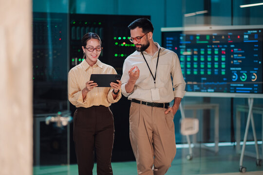 It professionals analyzing data on tablet and screen in server room, ensuring network security and cloud computing infrastructure