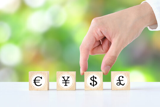 円やドルなどの様々な貨幣記号の中からドルを選ぶ人物の手―外貨預金や為替のイメージ