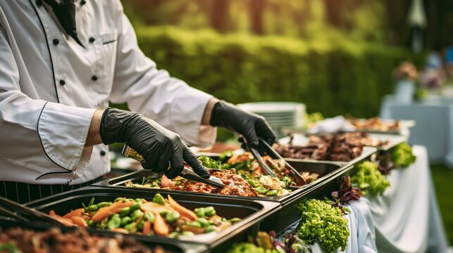 Professional chef in white uniform and black gloves serving gourmet food at outdoor buffet.