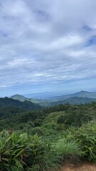 Fototapeta premium Vast Mountain Vista: A breathtaking panoramic view unfolds across a landscape of rolling, verdant mountains stretching towards a hazy horizon under a dramatic, cloud-filled sky.