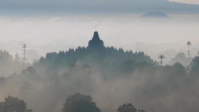 Ancient borobudur temple silhouette emerging from morning mist in central java indonesia.