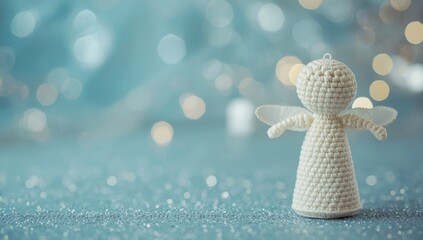 Fototapeta premium White crocheted angel figure with festive shimmering blue textured background and bokeh