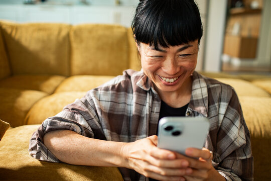 Smiling woman using smartphone on sofa at home