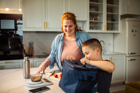 Mother helping son pack school lunch in home kitchen