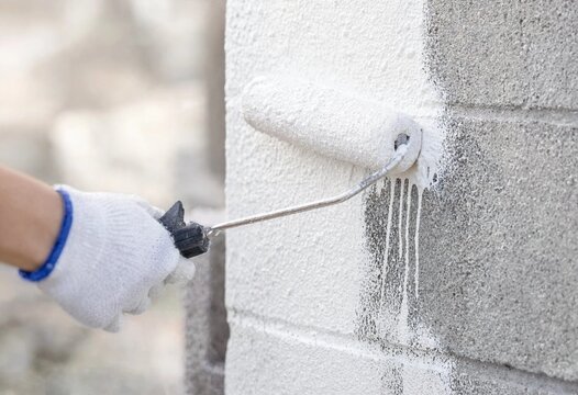 Professional worker applying primer to an exterior building wall during renovation, preparing textured concrete surfaces for durable paint adhesion, residential construction, maintenance.