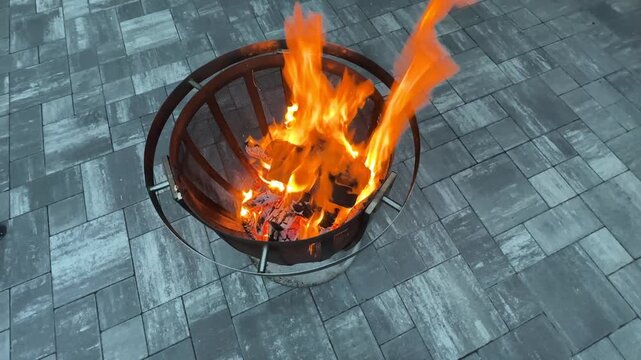 Fire burns in a metal pit on a stone patio during the evening hours