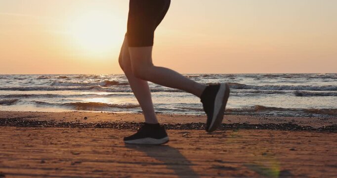 Legs close Up of woman running on the beach at sunset. Outdoor fitness and healthy lifestyle. Focus on water