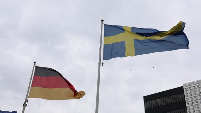German and Swedish flags waving in slow motion against a cloudy sky