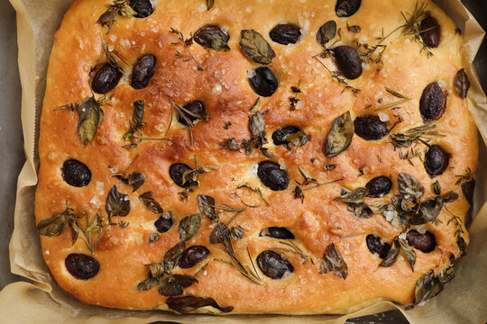 Freshly baked homemade Italian focaccia bread with rosemary, oregano, thyme, basil herbs, salt and black olives on top. Traditional Italian food, cuisine closeup, flatlay, top view, lunch background