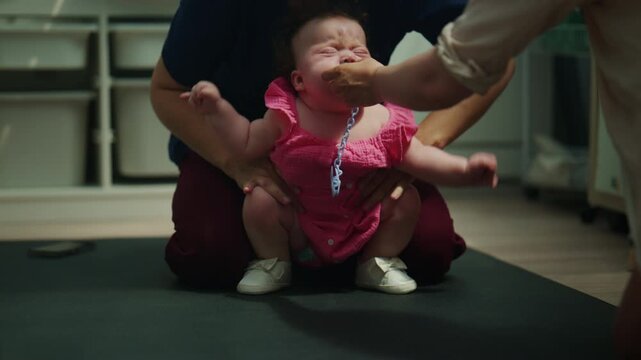 Baby practicing supported sitting on a padded therapy surface while caregivers provide stability and guidance, encouraging physical development and coordination